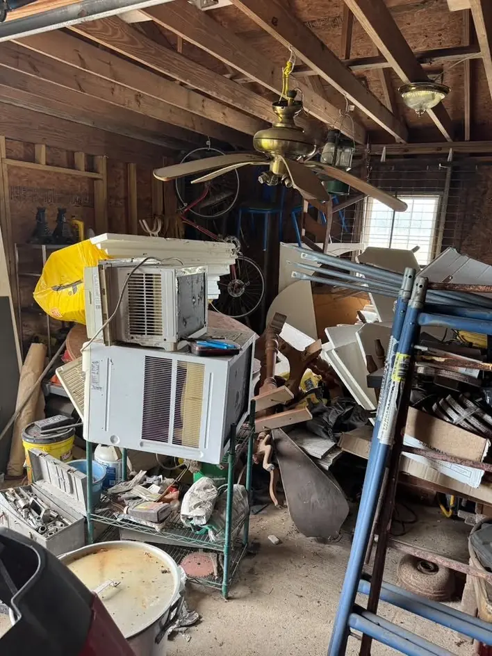 A garage packed with an air-conditioning unit, ladders and stored scrap