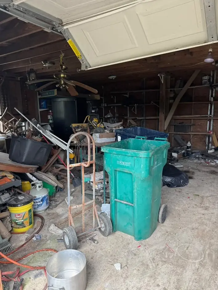 A garage part way through clearing, with a wheelie bin and hand truck