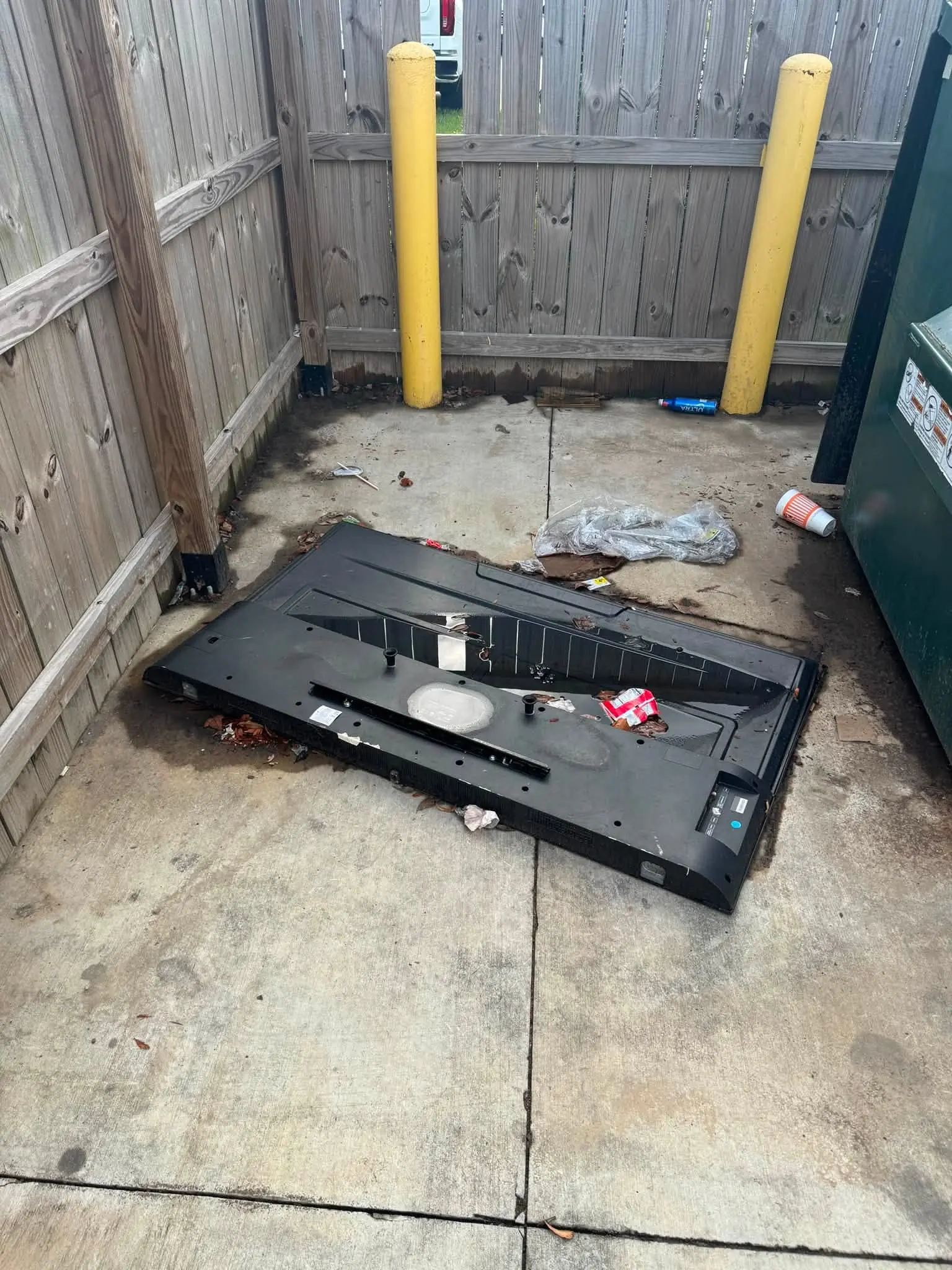 A large flat-screen television dumped on the concrete beside a commercial dumpster