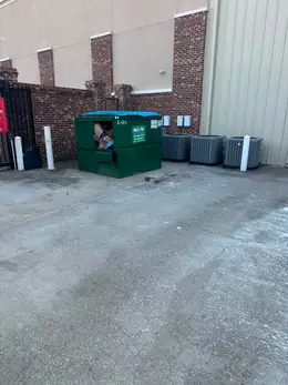 A commercial dumpster and air-conditioning units on the concrete behind a business