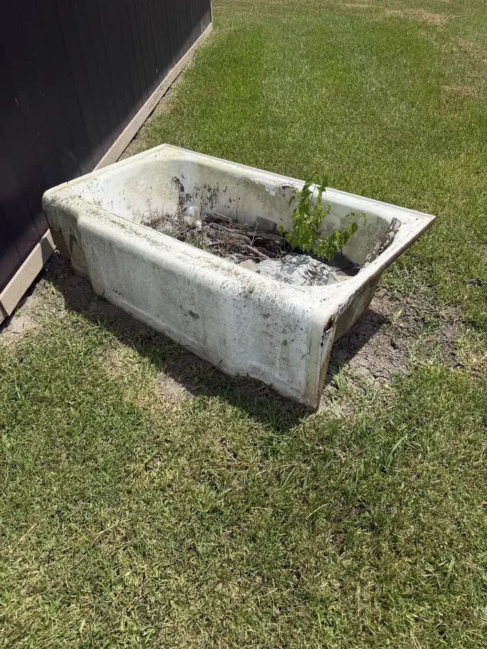Old cast-iron bathtub sitting on a lawn beside a shed before removal