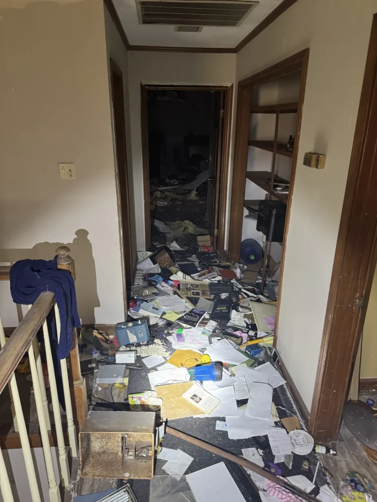 A bedroom in a vacated property strewn with paperwork, clothing and household debris before clearing