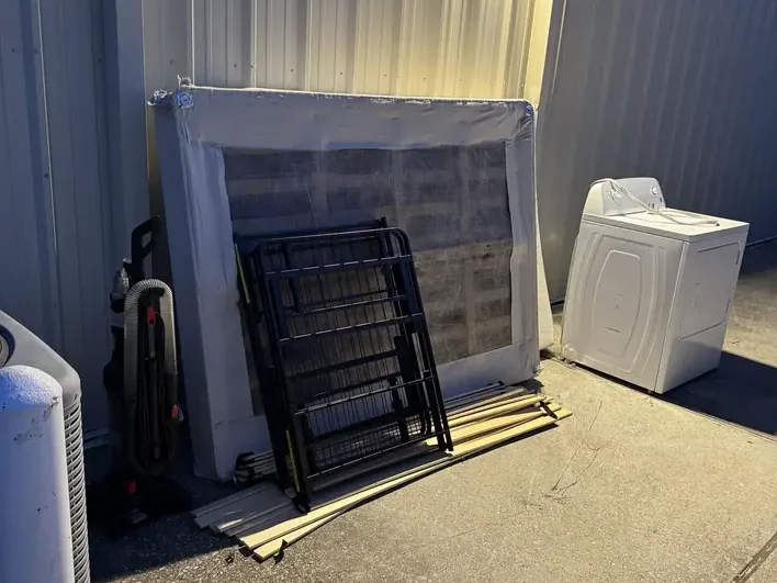 A box spring, a folding metal frame, a washing machine and a vacuum set out together beside a building for one pickup