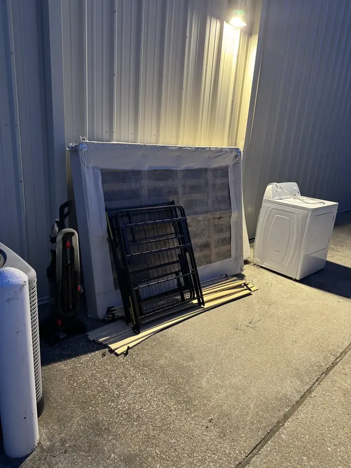 Mattress, folding chairs, a washing machine and a vacuum set out beside a building