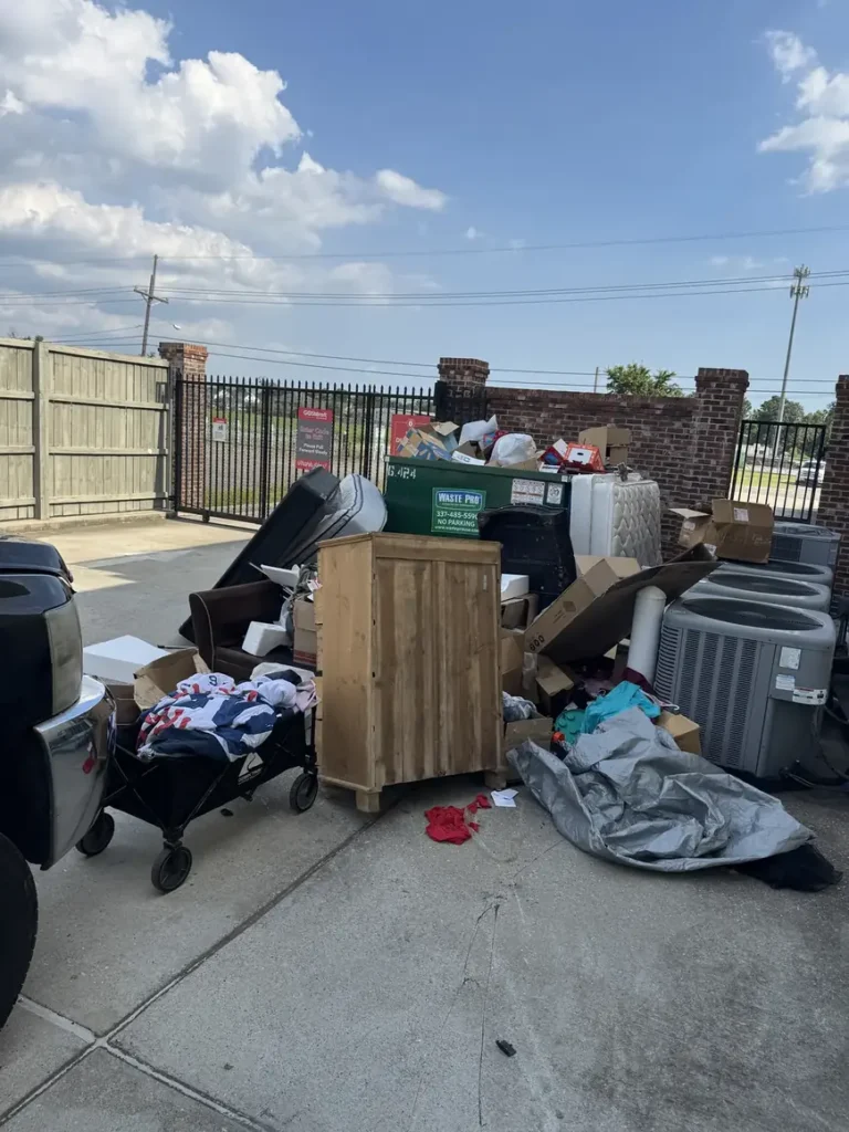 Furniture, boxes and air conditioning units piled beside a dumpster enclosure