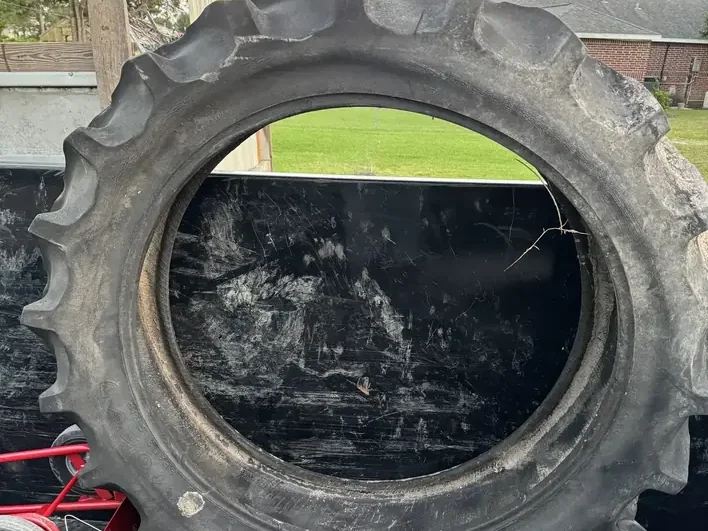 A large tractor tire loaded upright in the Klutter Krewe dump trailer, with a red hand truck beside it