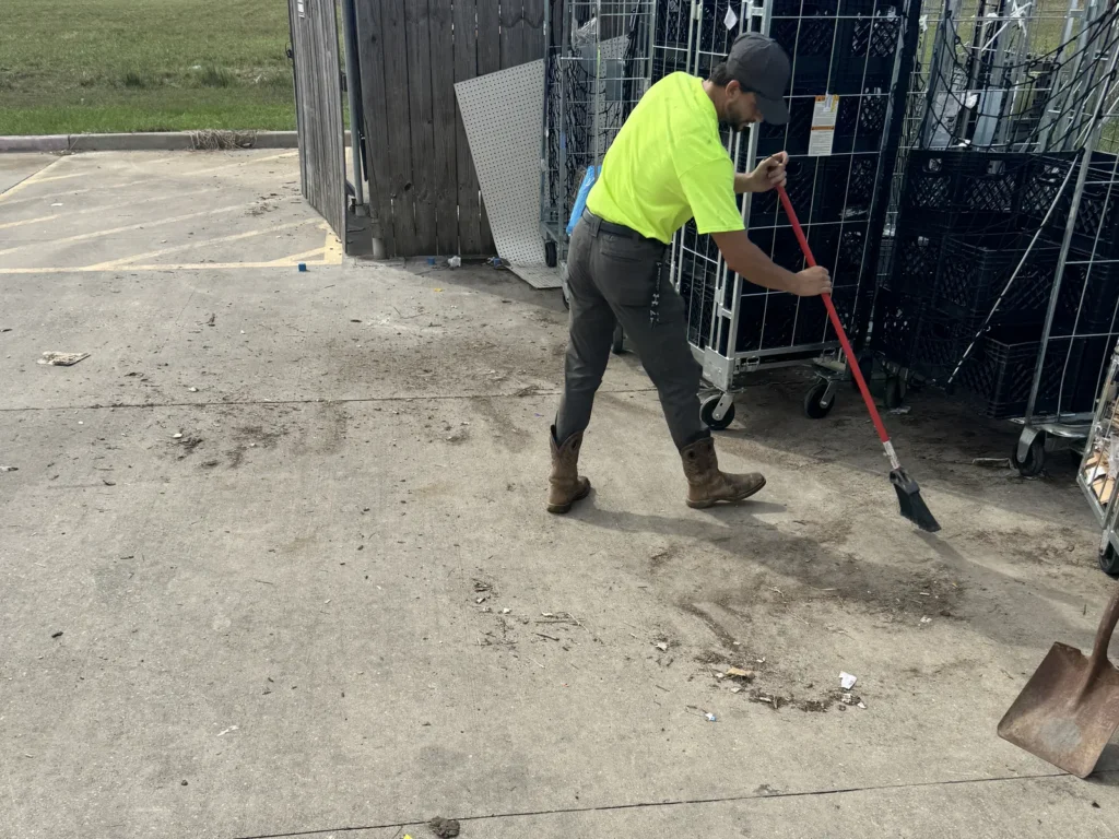 A crew member sweeping the cleared concrete of the dumpster corral after cleanup