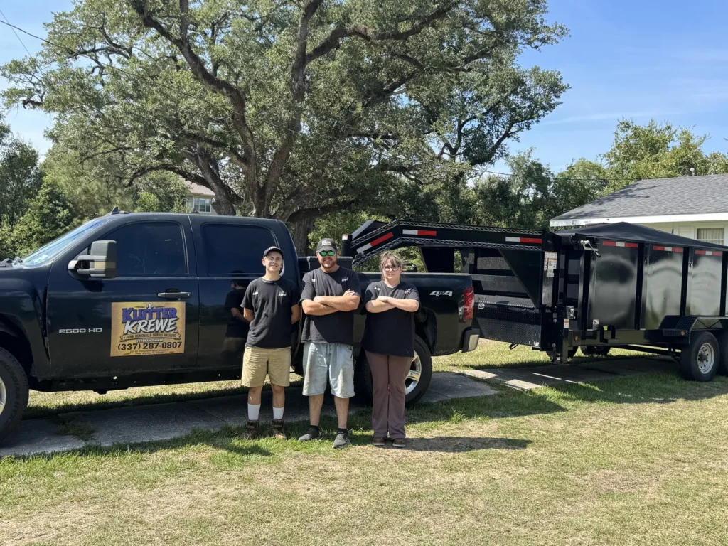 Three Klutter Krewe crew members standing beside the company truck and dump trailer in Lake Charles