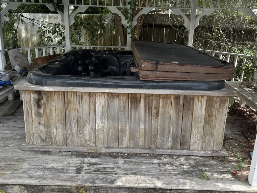 A hot tub in a wood surround under a backyard gazebo in Rayne before demolition and removal